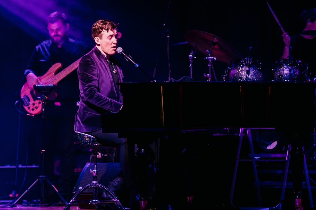 A man singing in a microphone while sitting at a piano