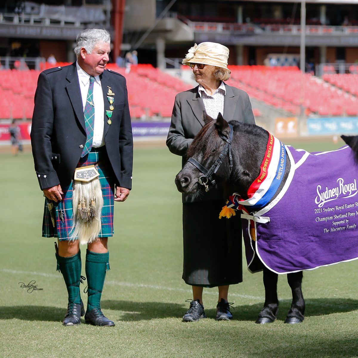 Man in kilt with woman in hat and pony in show ring