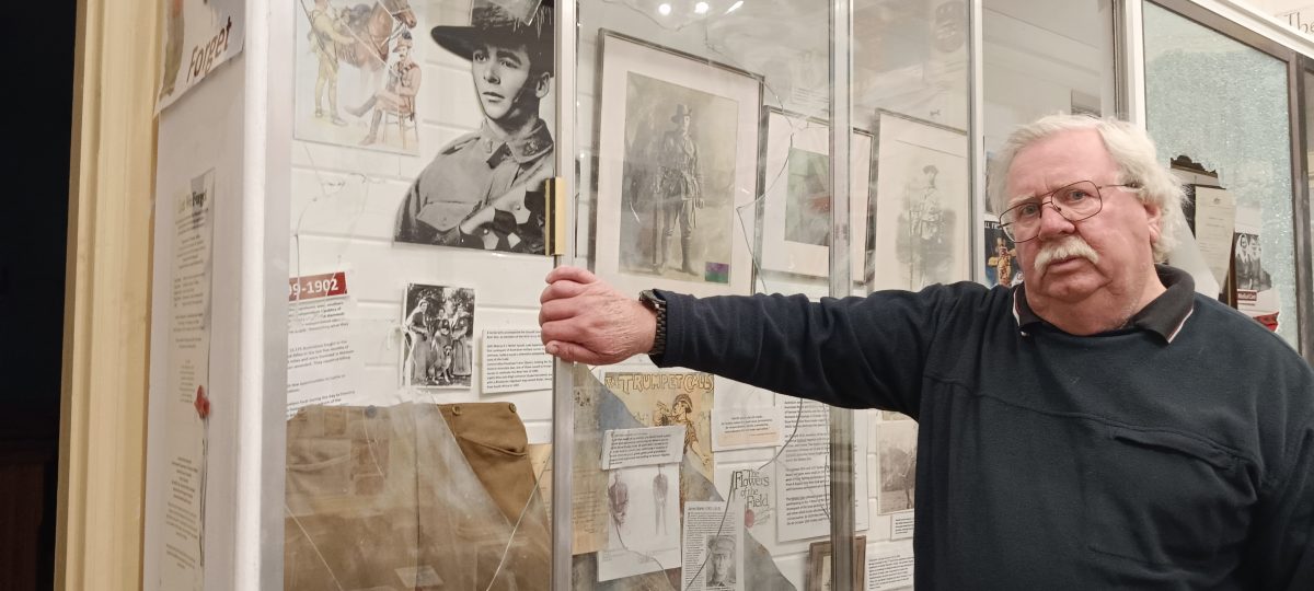 Man standing in front of wall of photographs damaged by vandals