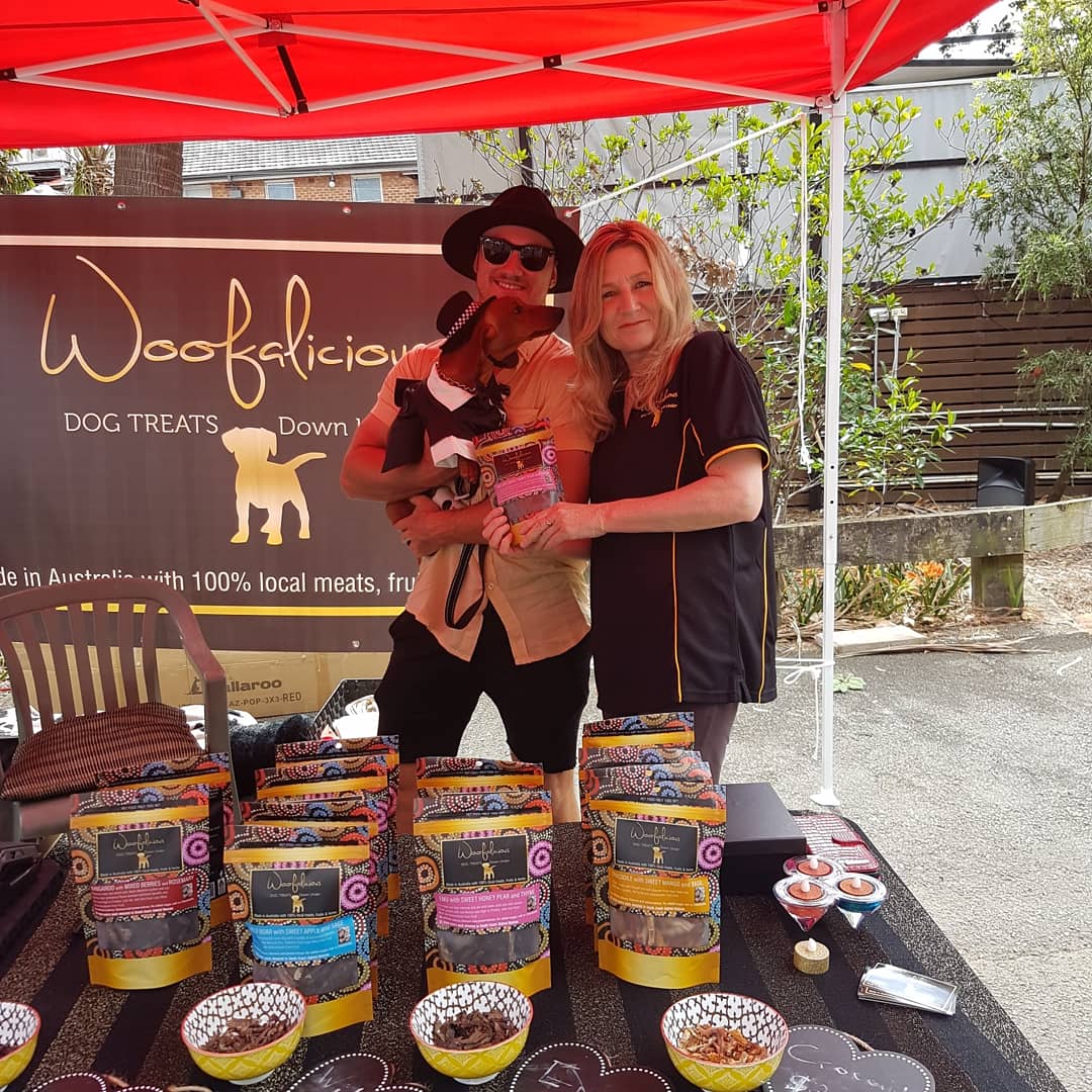 Two people standing and holding a dog in front of a table of dog treats