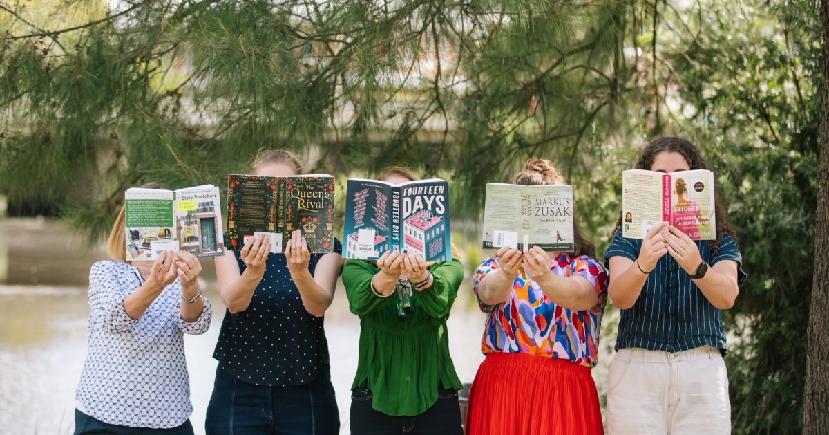 Five people standing in a line and holding open books in front of their faces