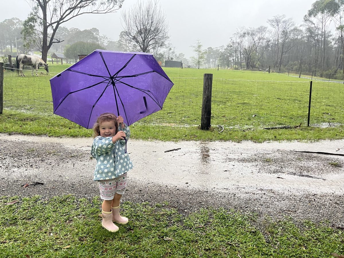 little girl standing in the rain holding an umbrella