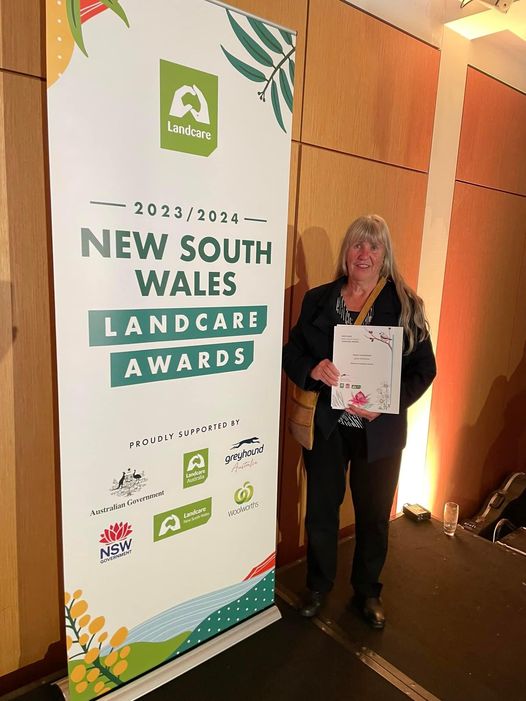Woman with award in front of NSW Landcare awards sign