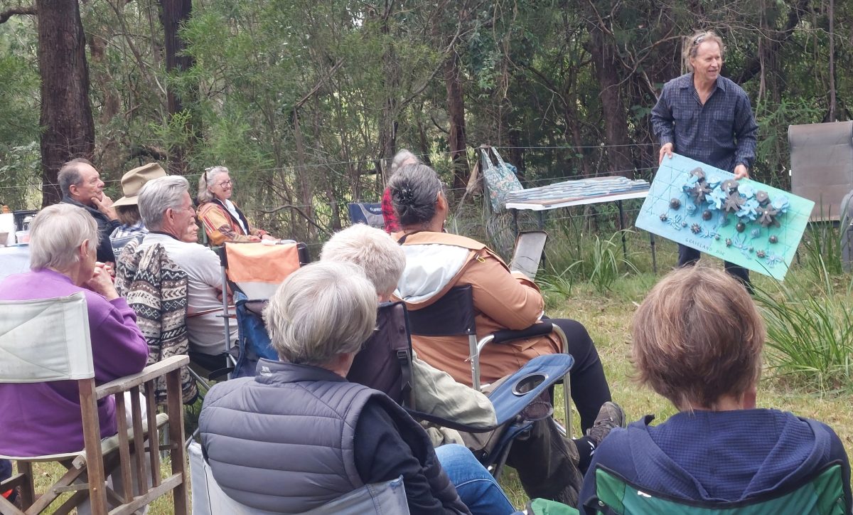 man giving a talk to a seated group in a bushland setting