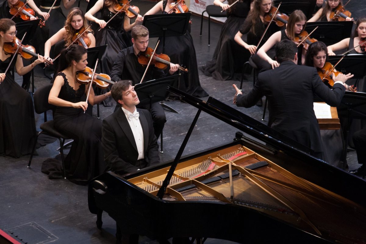 A man sitting at a piano surrounded by people playing instruments