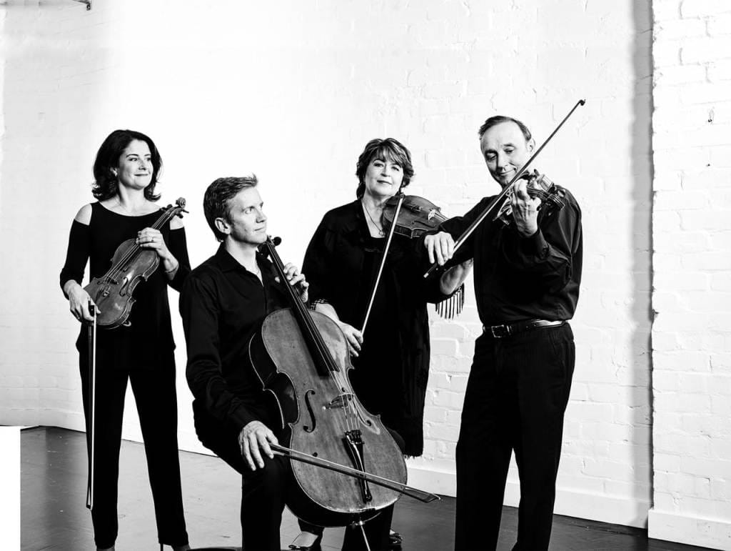 A black-and-white image of four musicians with their instruments