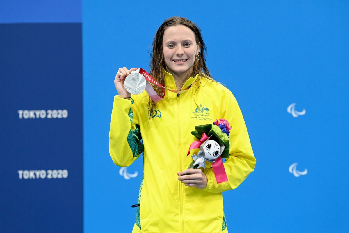 A young woman in a yellow jacket holding flowers and a silver medal