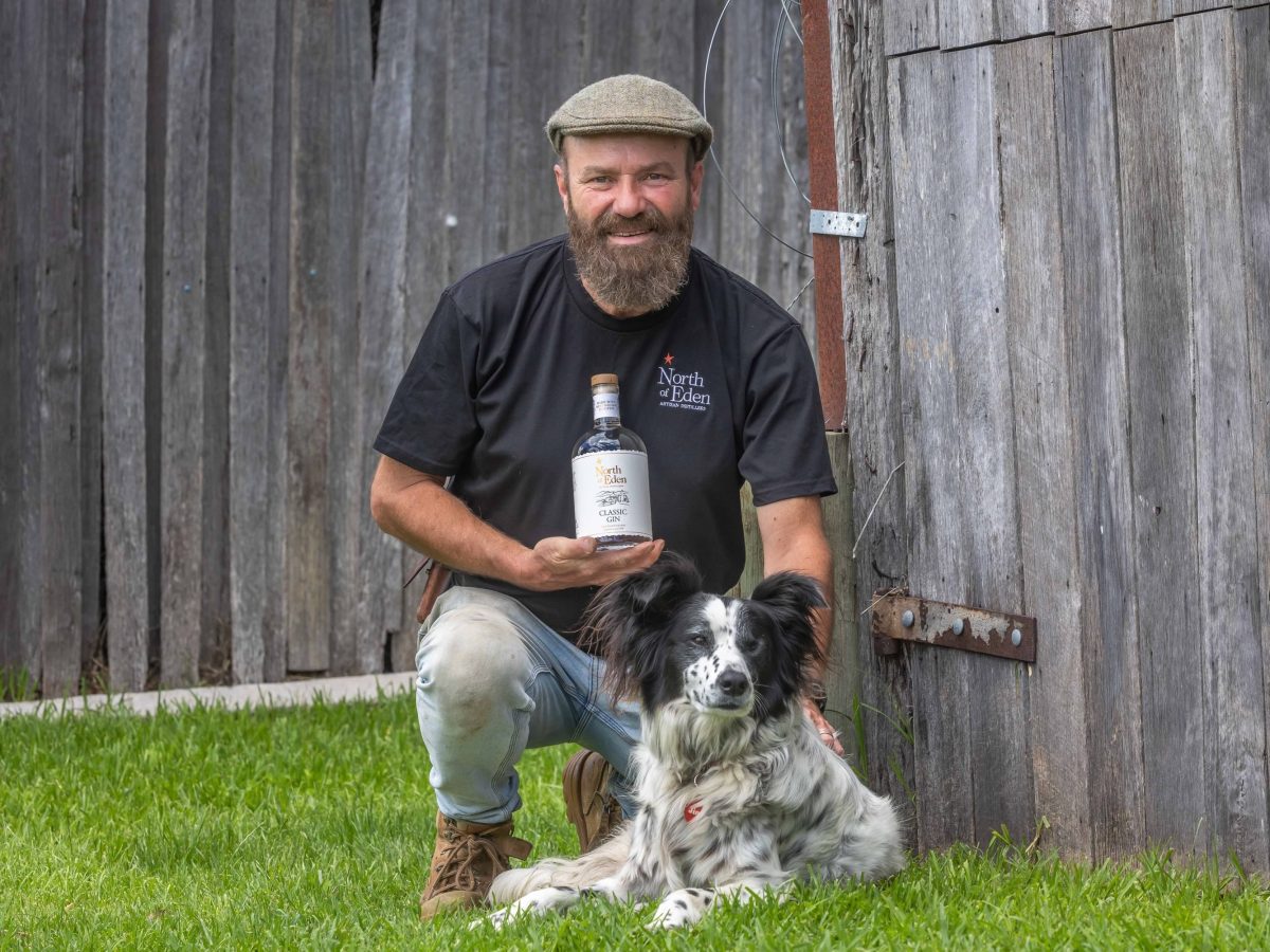 A man holding a bottle of gin kneeling next to a dog