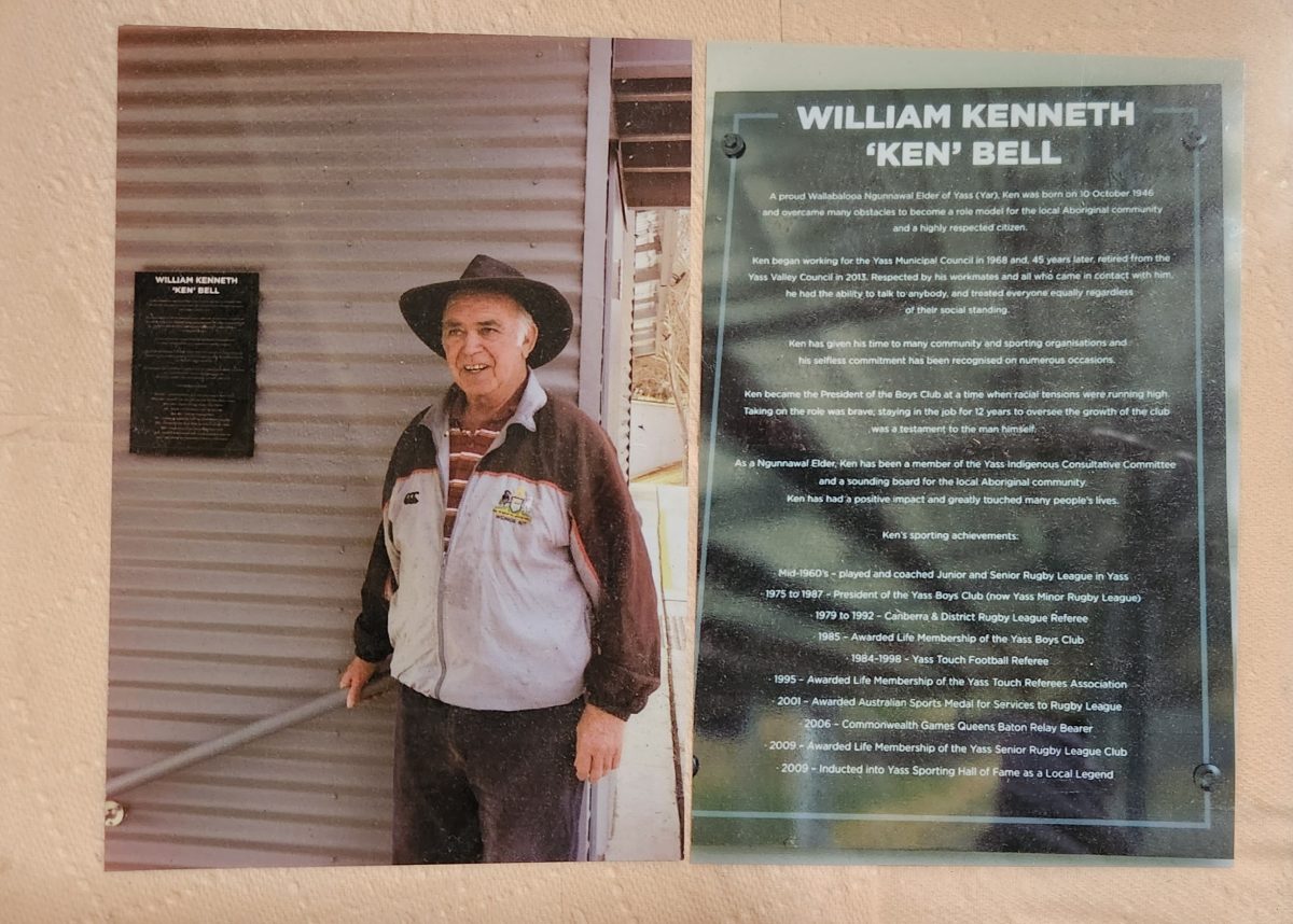 Man in hat in front of tribute board to William Kenneth 'Ken' Bell
