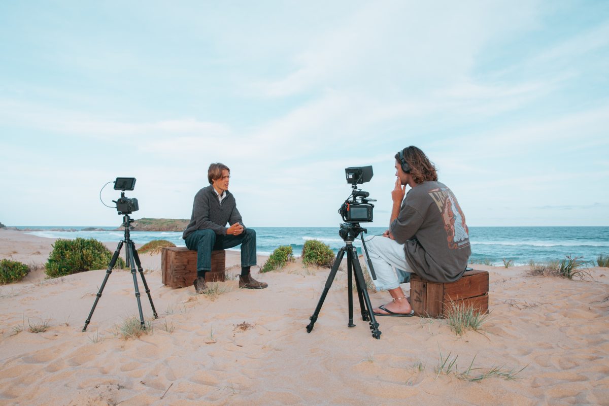 two men filming an interview on a South Coast beach