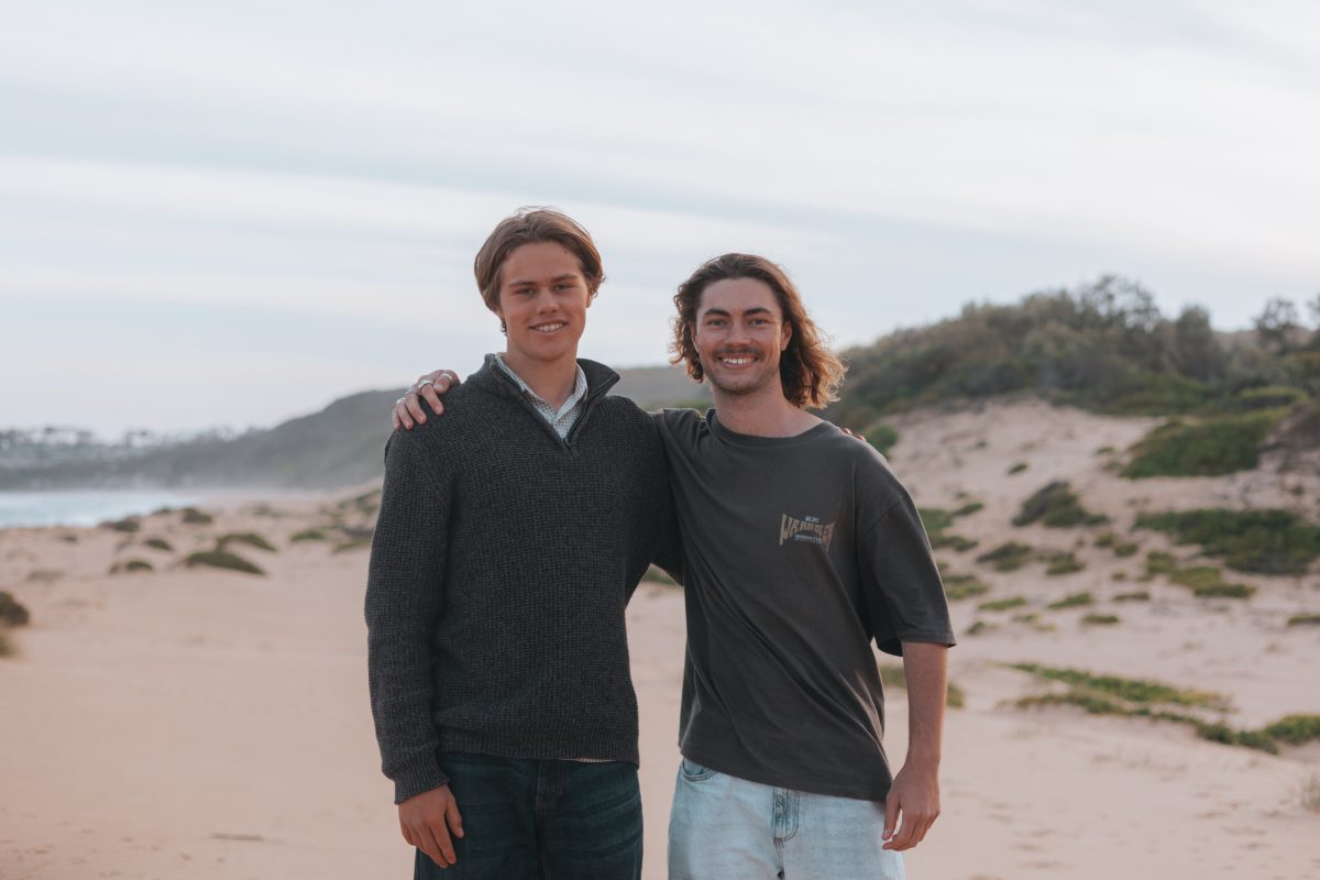 Jacob Shields and Jordan Mundey with their arms around each other on a beach