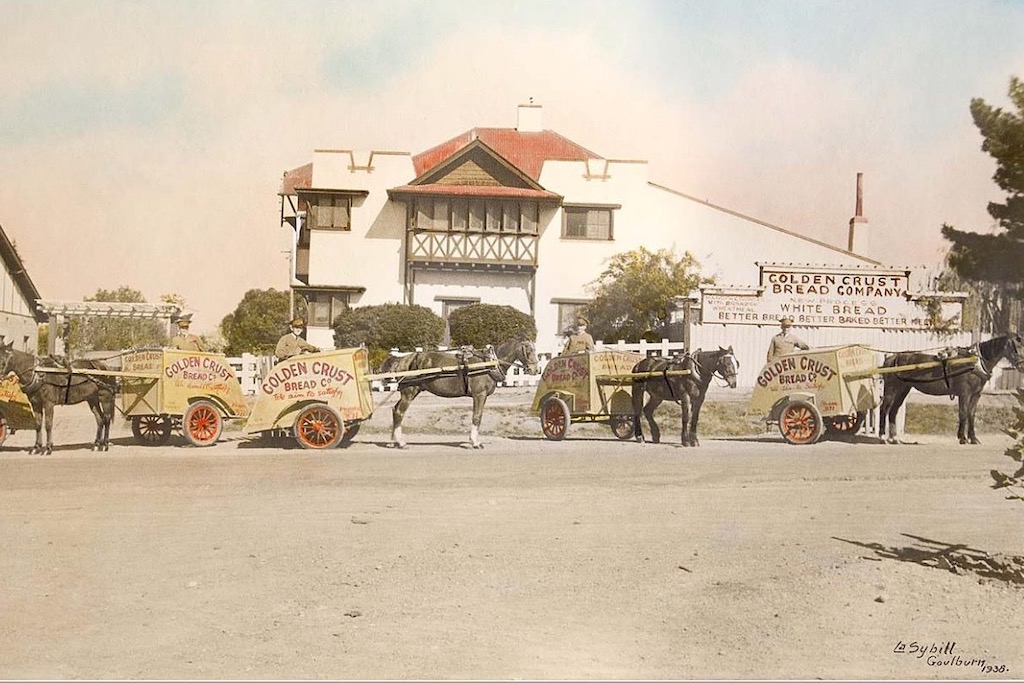 old photo of horses, carts and riders in front of a business