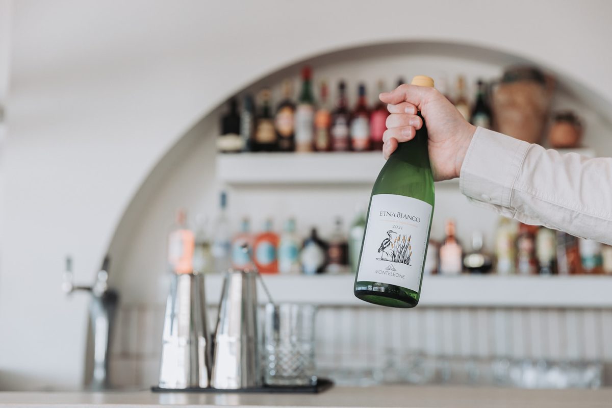 A hand holds a bottle of wine with a bar in the background. 