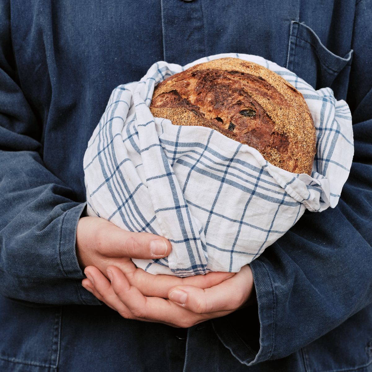 Person in dark-blue linen holds a loaf of bread wrapped in a tea towel