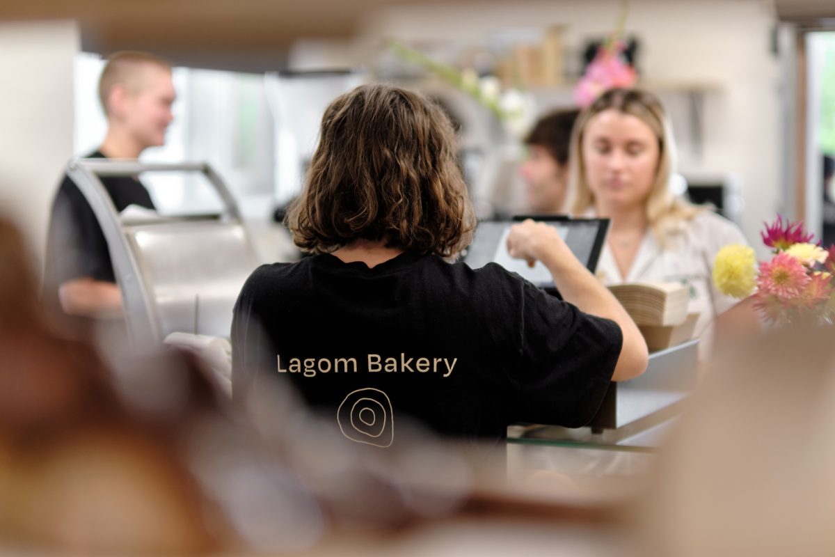 Shot from behind as a staff member serves a customer, showing off the Lagom Bakery logo of three oddly shaped nested circles.