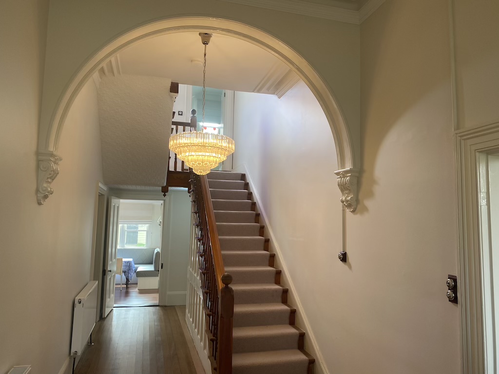 The lobby entrance opens to an ornate archway and timber staircase which leads to upstairs bedrooms.