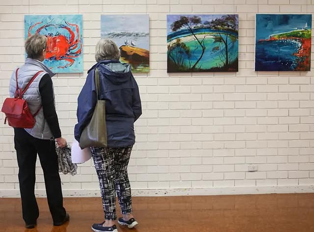 Two women view a wall of art at Escape ARTfest