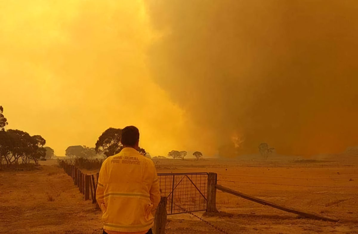 A firefighter looks at smoke under an orange sky