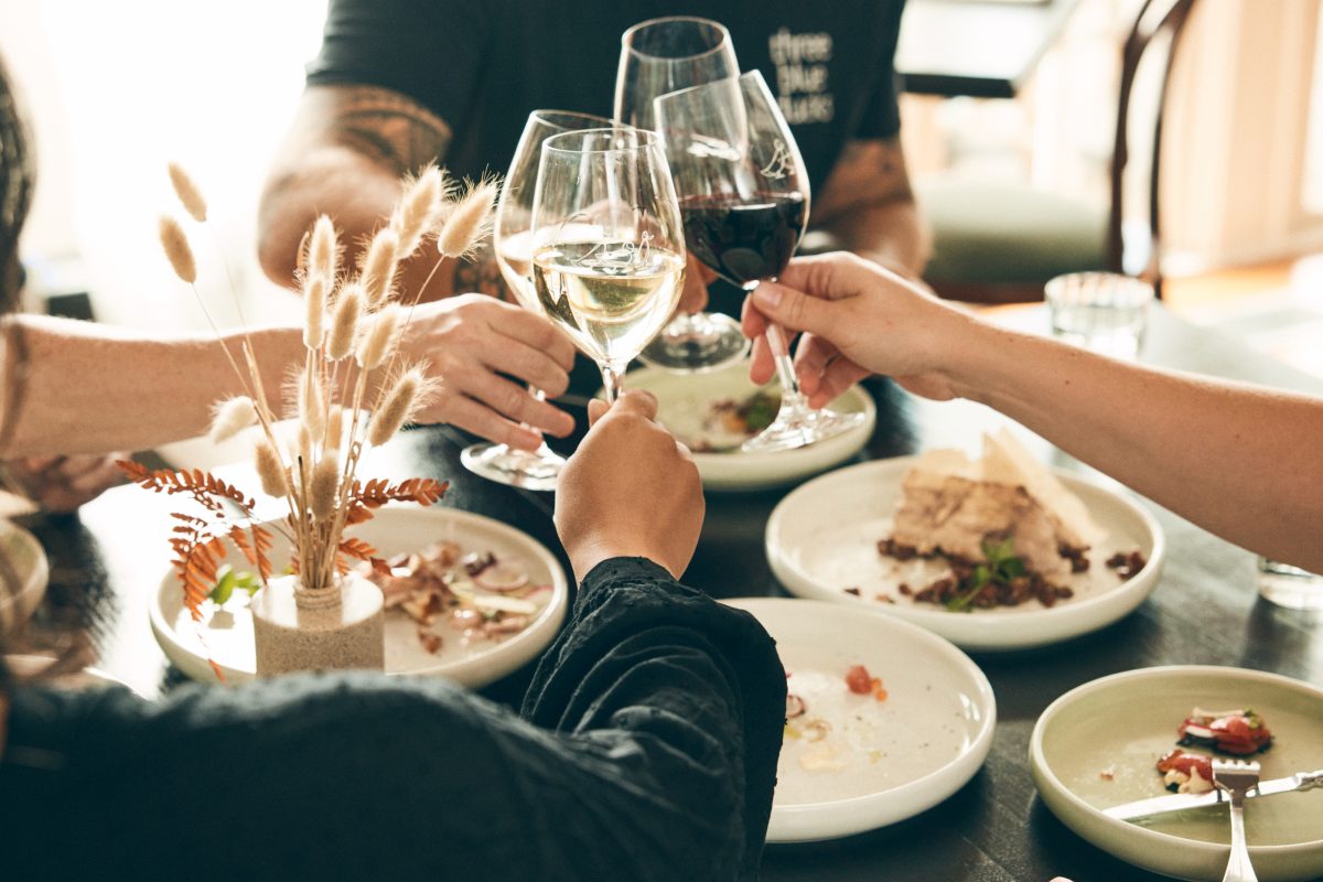 A group of people at a lunch table clink their wineglasses together,