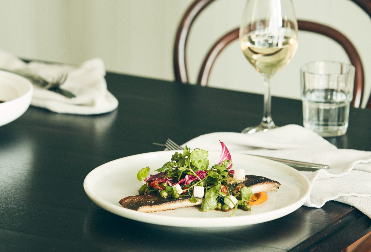 A plate of trout on a black restaurant table with a glass of white wine. 