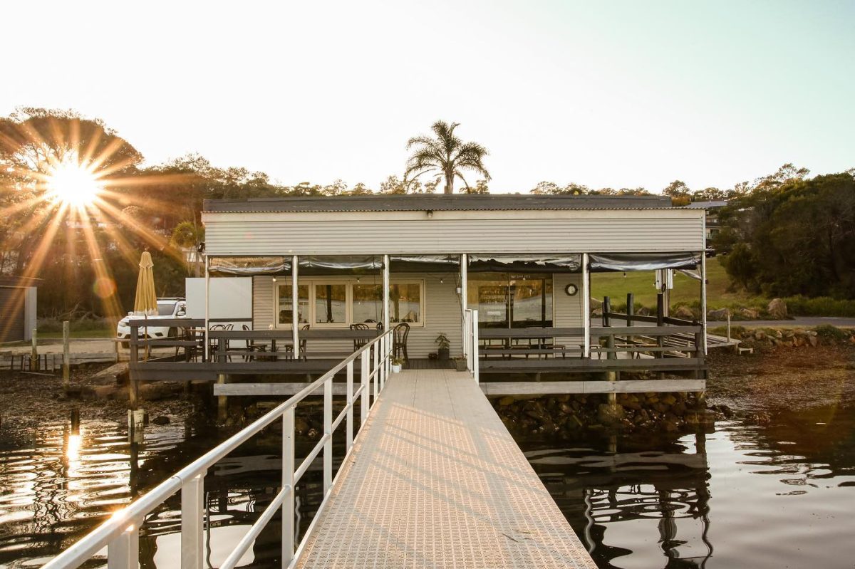 A shot of a small building attached to a jetty on the water, with the sun in one corner.