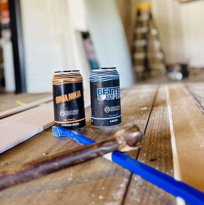 Two Tumut River branded tinnies of beer on a table with tools.