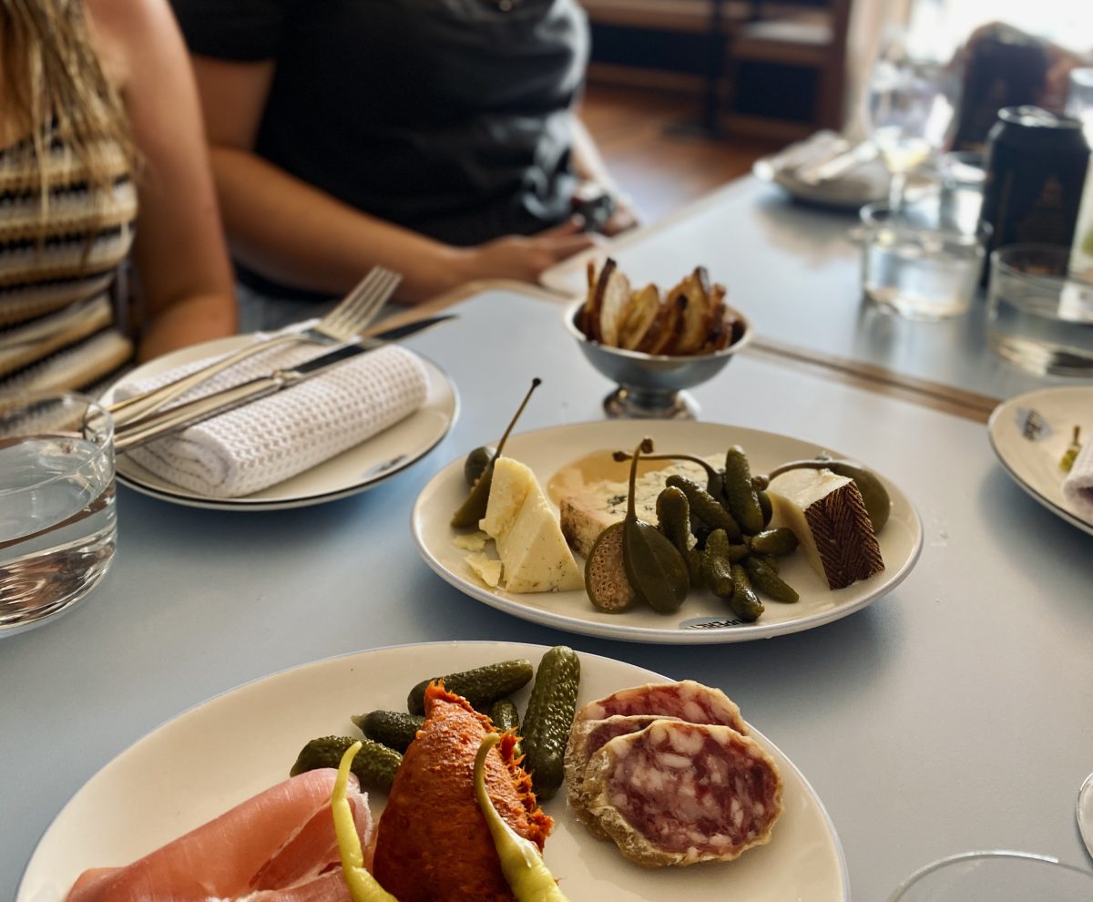 Two plates, one with charcuterie and cornichon pickles, and a cheese plate with caperberries