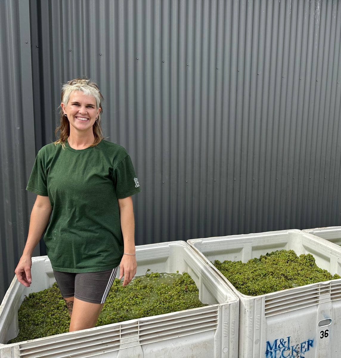 A woman with a funky haircut stands inside a large bin of green grapes