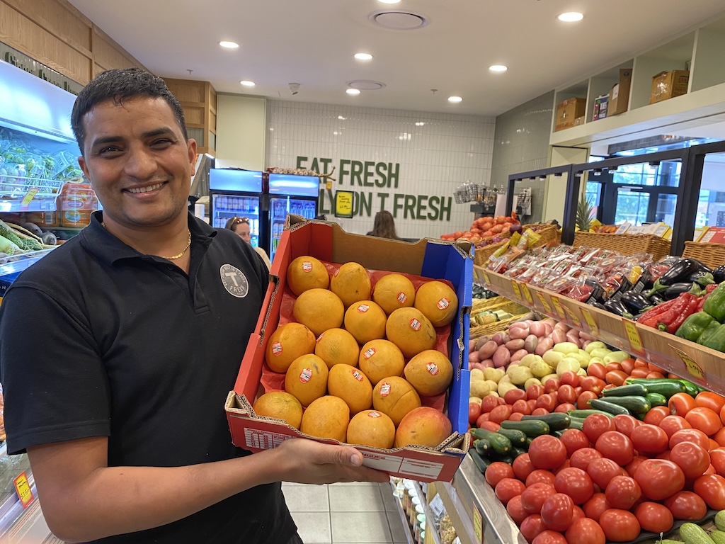 a man holding a tray of mangoes in a fruit shop