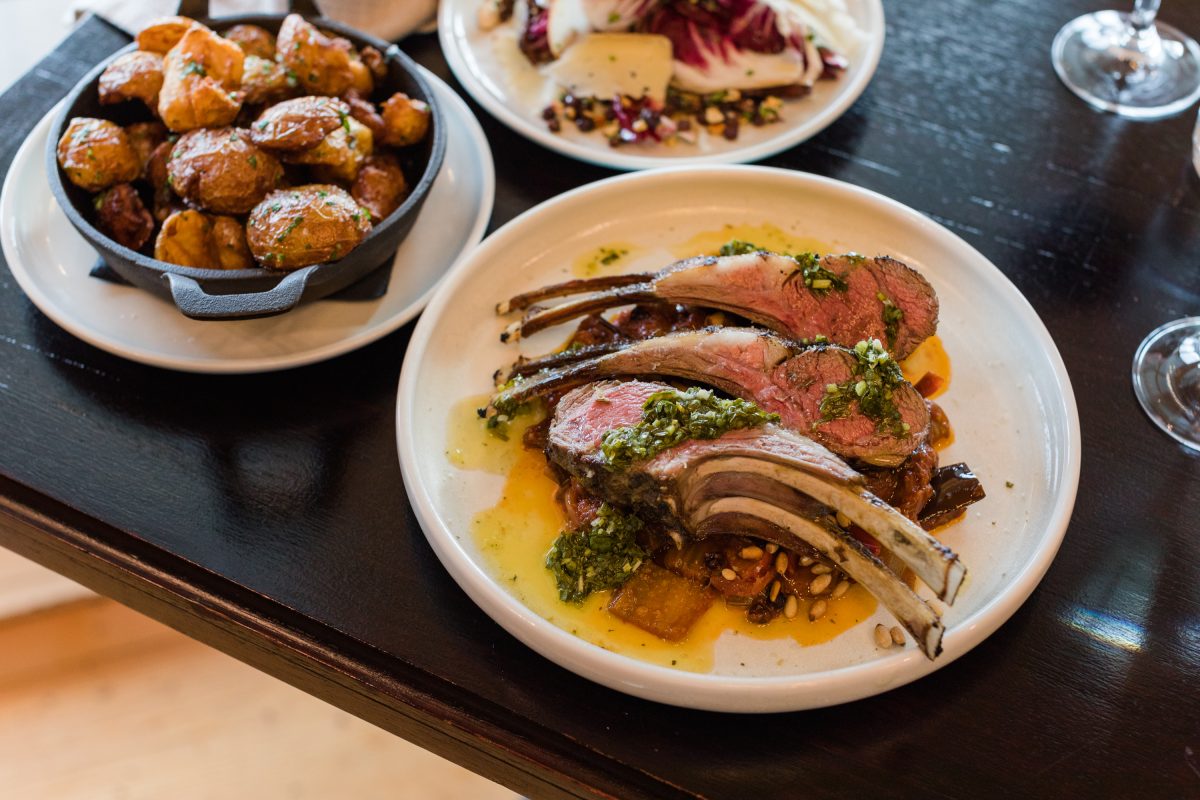 A tasty looking plate of lamb chops, and a bowl of potatoes on a black restaurant table.