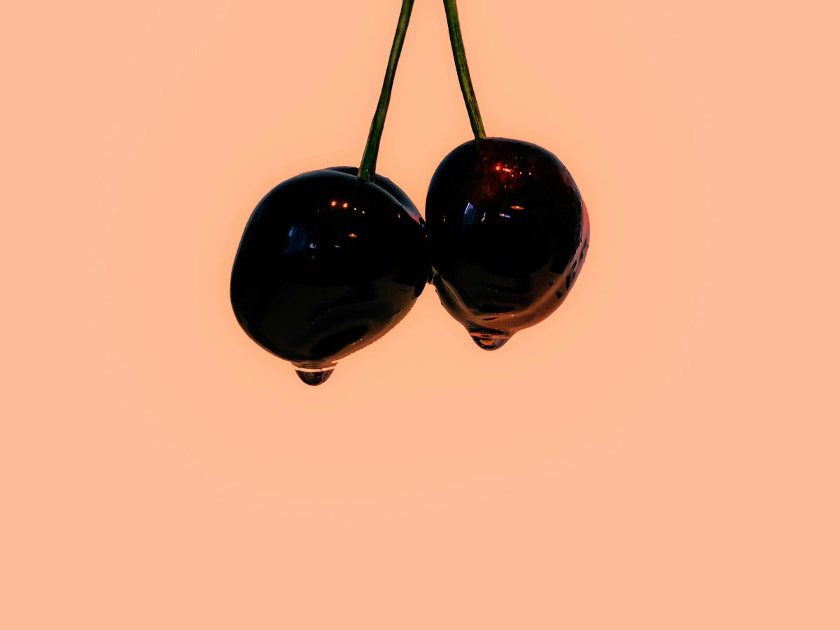 an image of two black cherries against an orange background