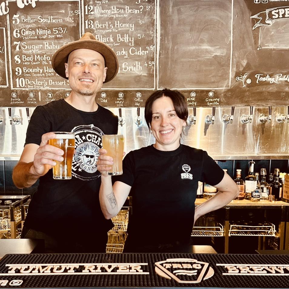 A man in a hat and woman hold up beers.