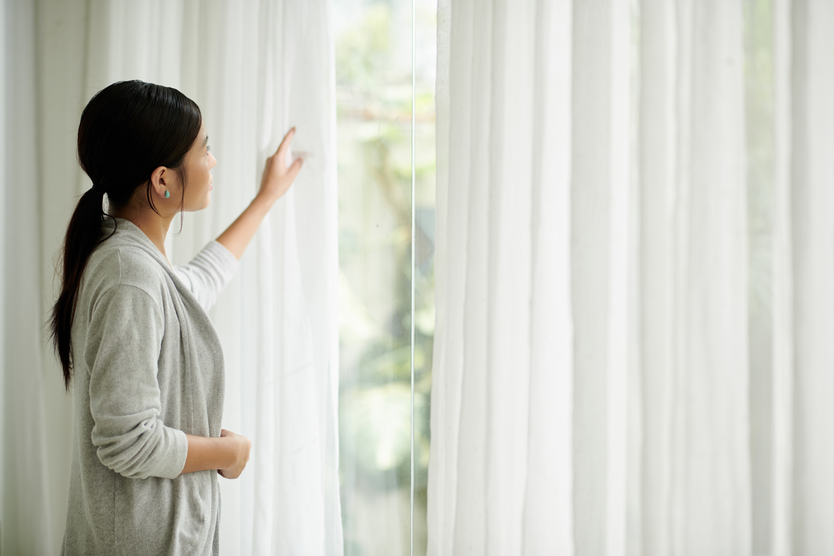 a person opening sheer curtains, looking out a window