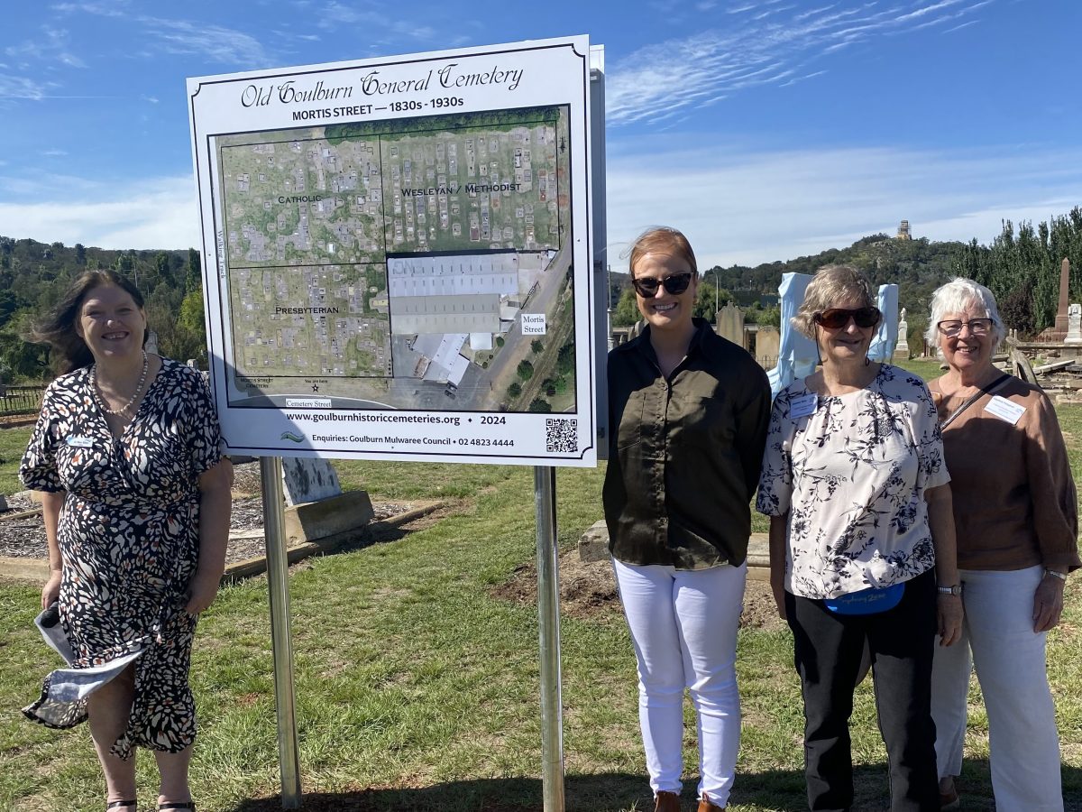 four women and a sign at a cemetery