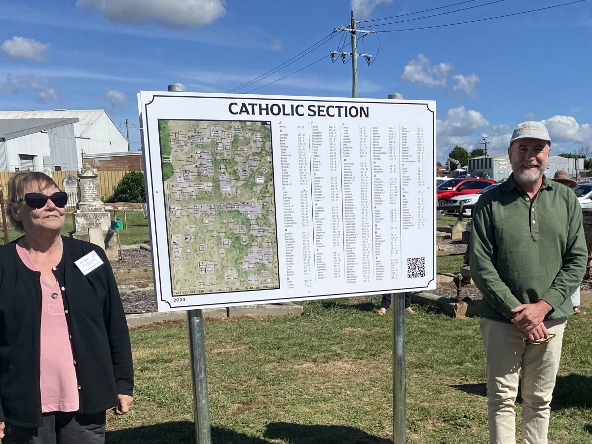 a woman and a man stand at a cemetery sign