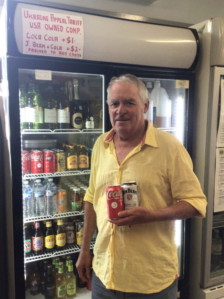 A man standing in front of a cafe fridge holding two cans of drink