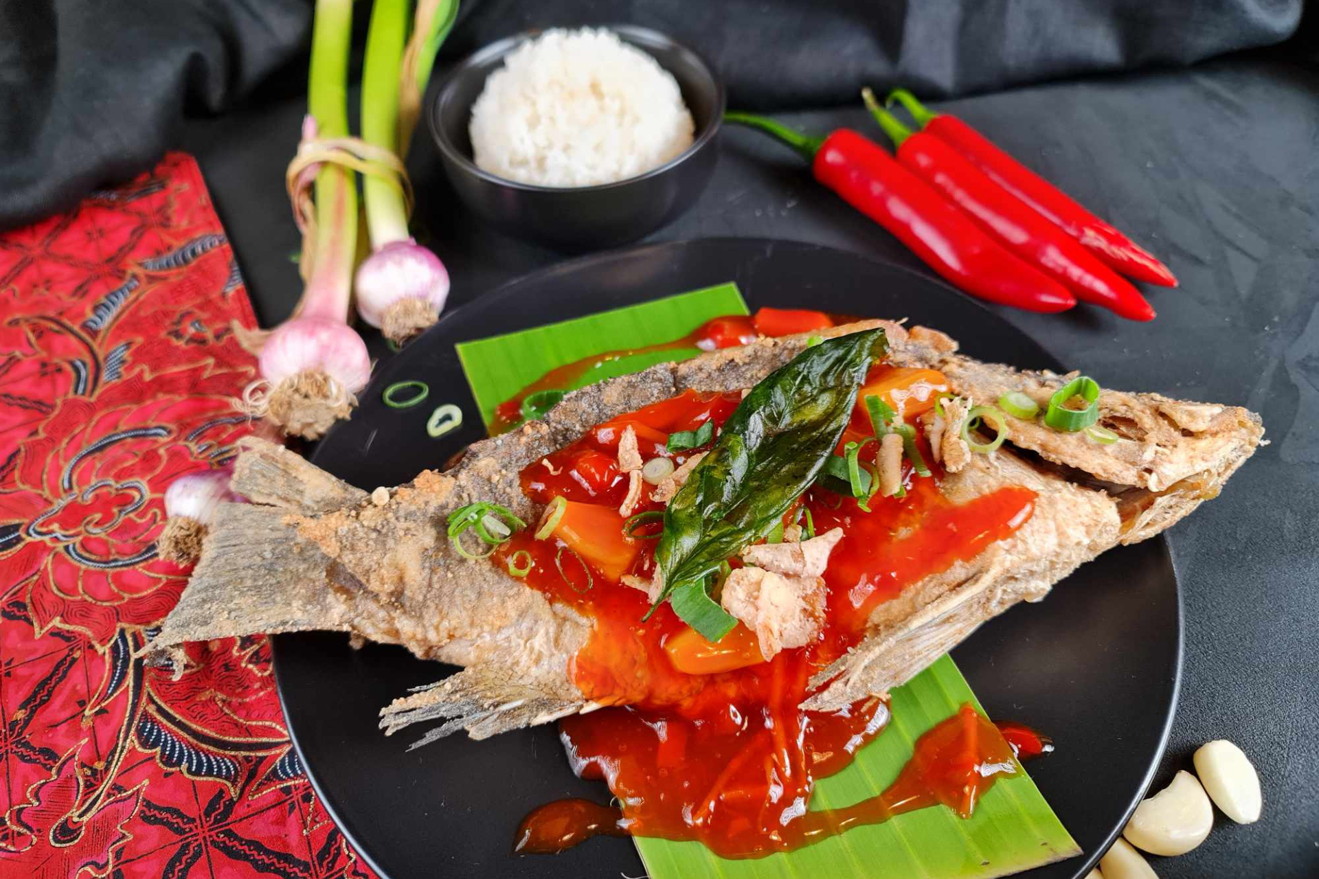 A whole cooked fish on a plate topped with sauce and vegetables.