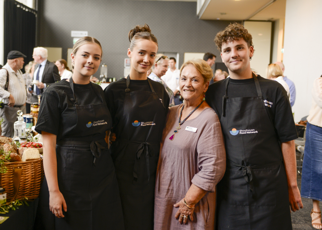 Three young adults in black T-shirts and aprons stand with an older woman