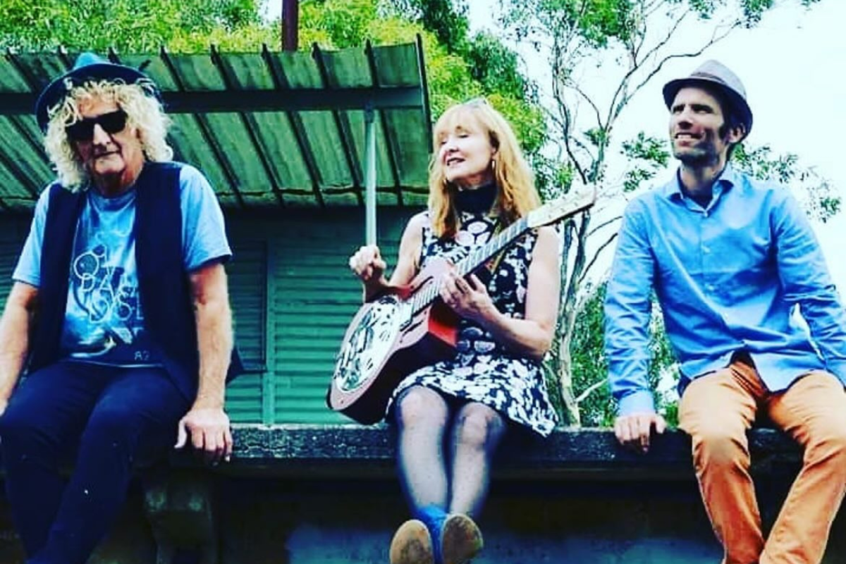 3 musicians sitting on the edge of an outdoor stage.