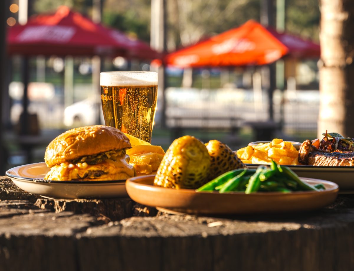 A burger and beer in foreground, with a fenced beer garden in the background.