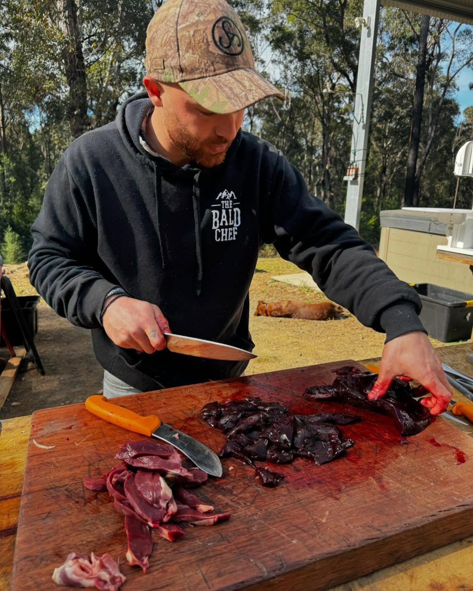 A man cutting up meat on a wooden chopping board