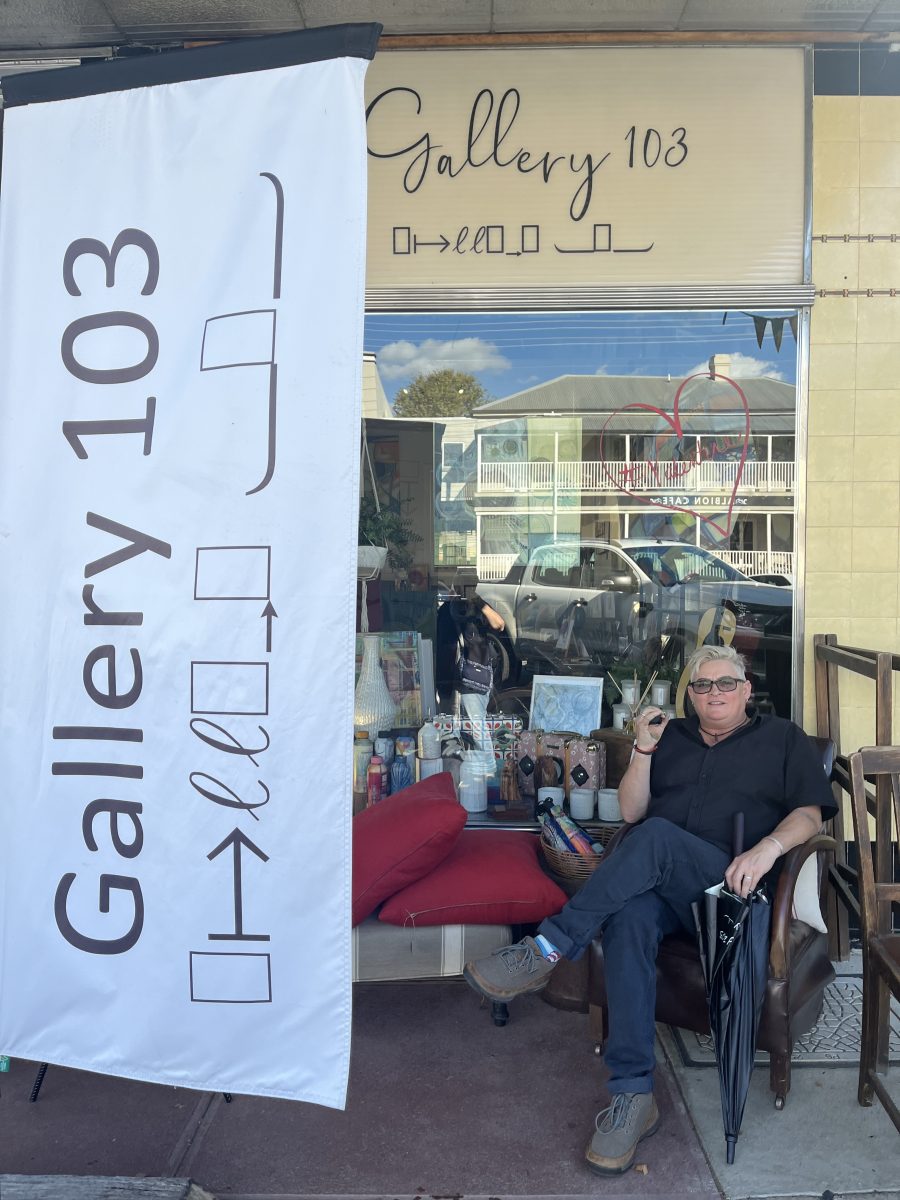 A woman sitting in a chair next to a banner advertising her gallery