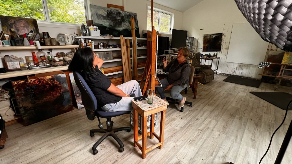 A woman sketching another woman, while both sit in chairs