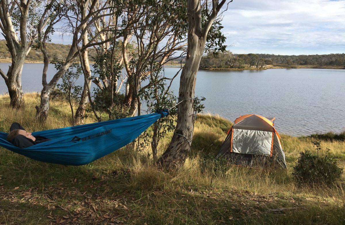girl in a hammock with tent and lake in background