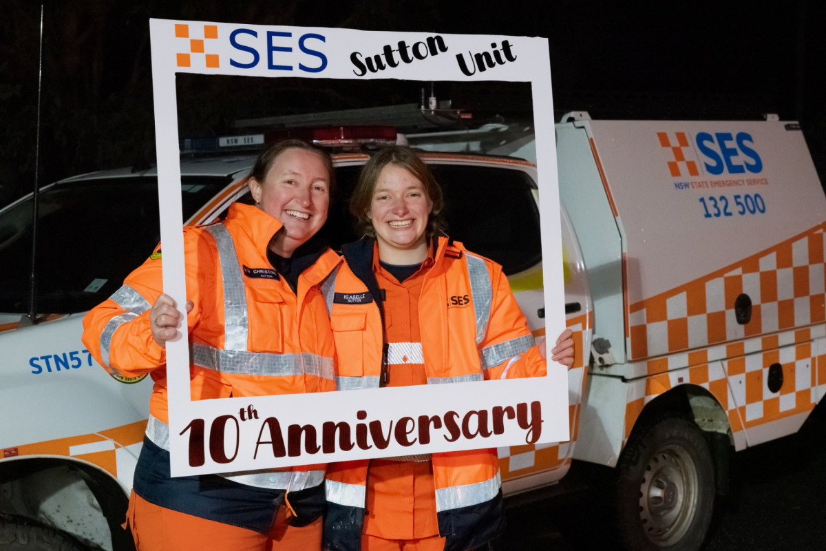 Two women in orange uniforms stand behind a banner