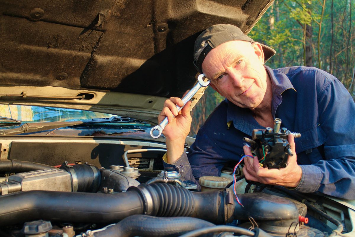 man under a car bonnet and working on an engine