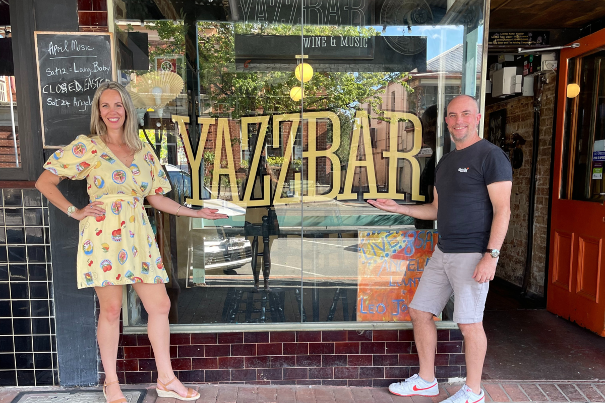 Man and woman stand in front of bar window.