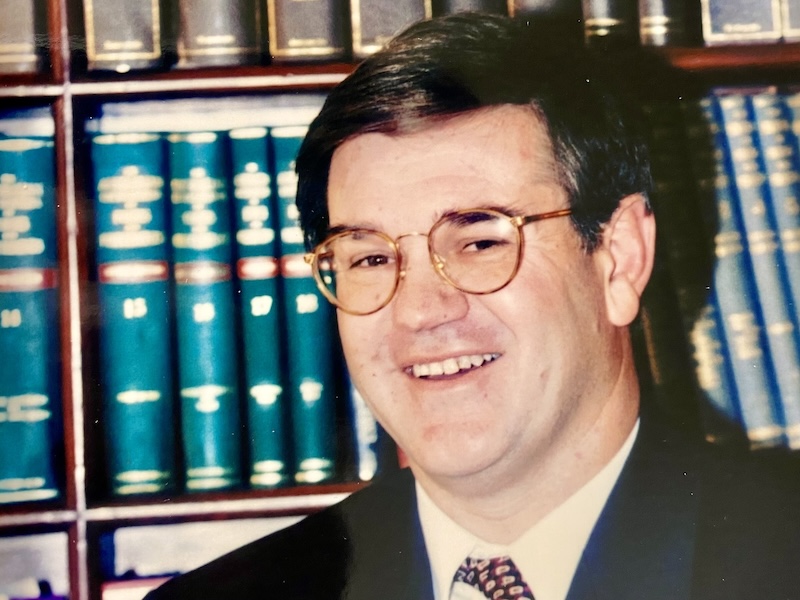 old photo of a smiling man standing in front of a book shelf