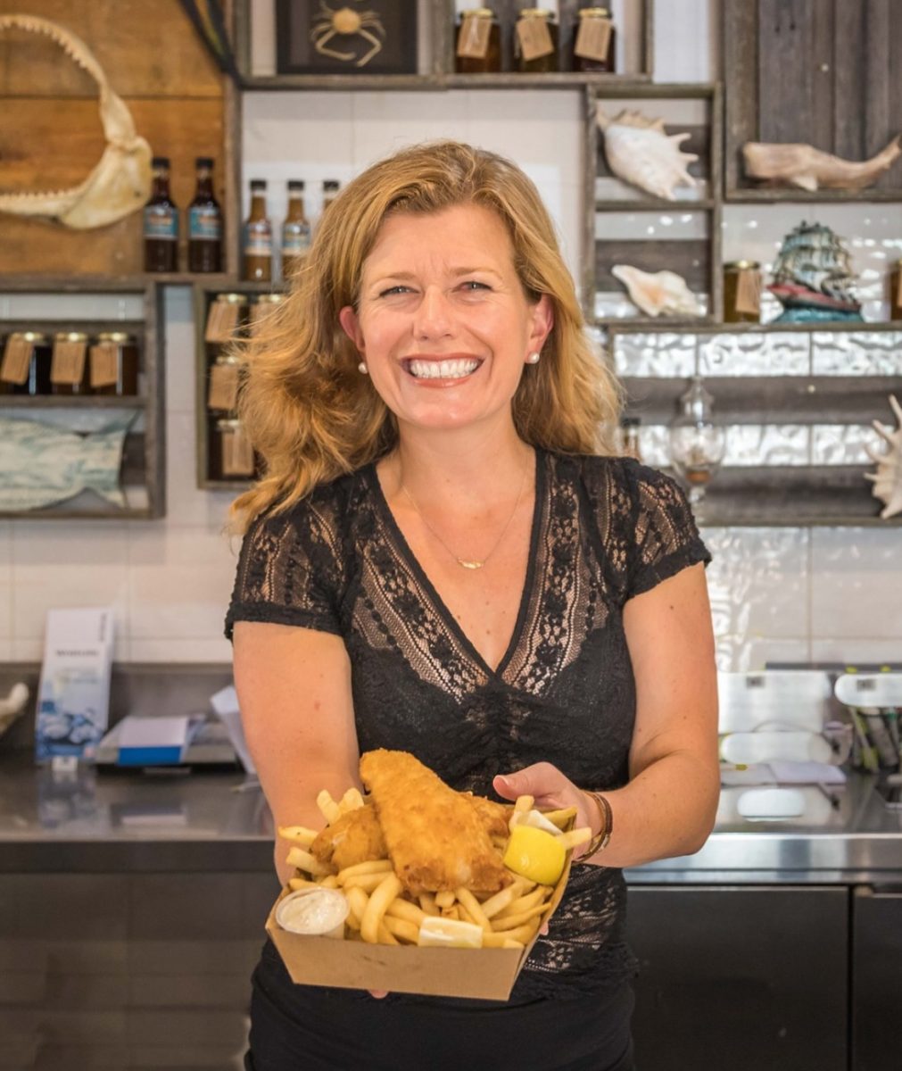 A smiling woman holding a takeaway box of fish and chips
