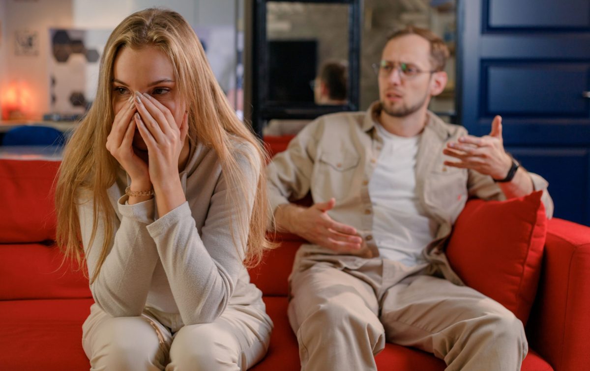 woman looking stressed on a couch while a man argues with her